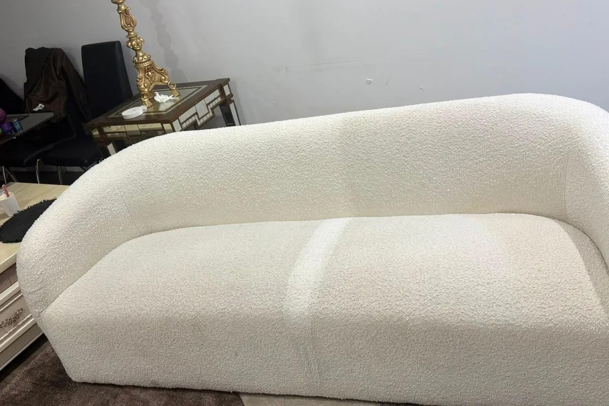 A cream boucle sofa partway through steam cleaning, the left half brighter than the right