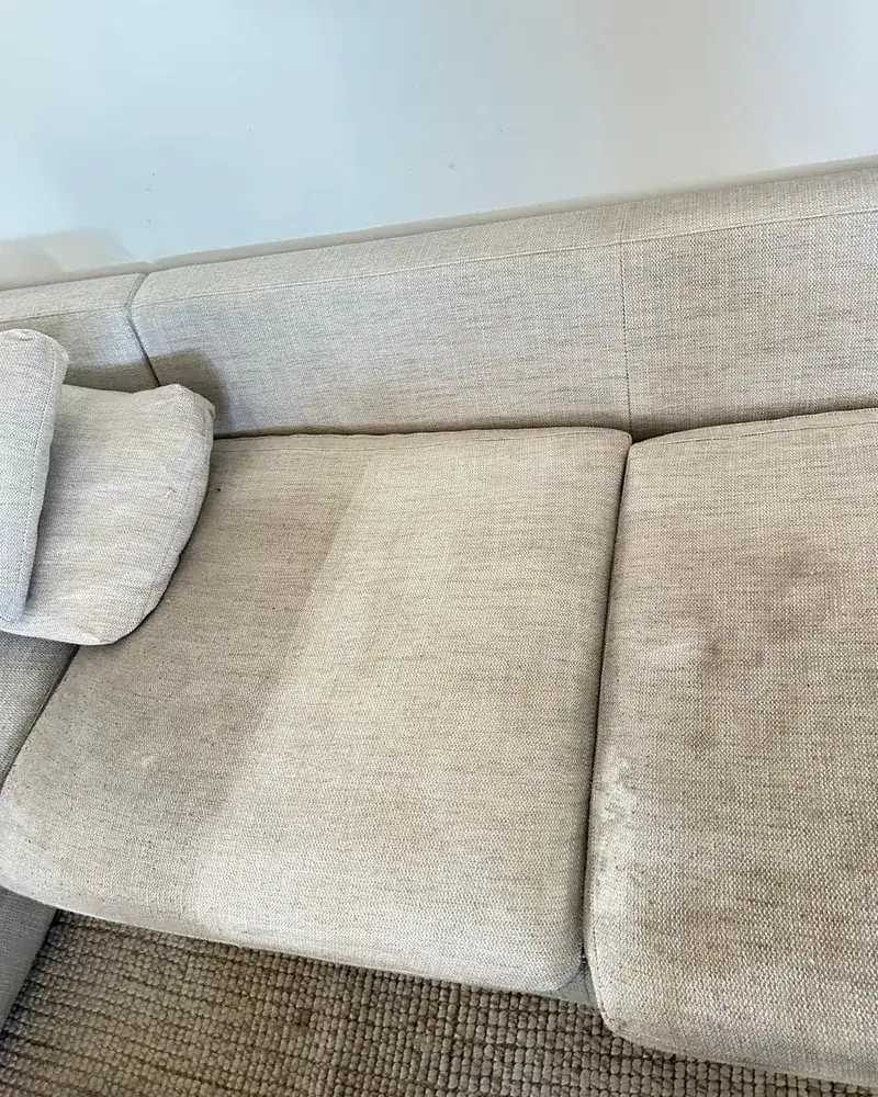 A fabric couch seat with one cushion cleaned pale and the next still stained dark