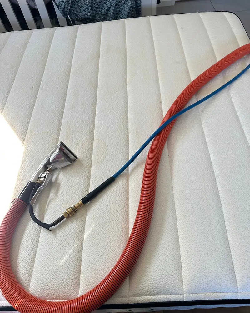A mattress being steam cleaned with the upholstery tool and hoses resting on it